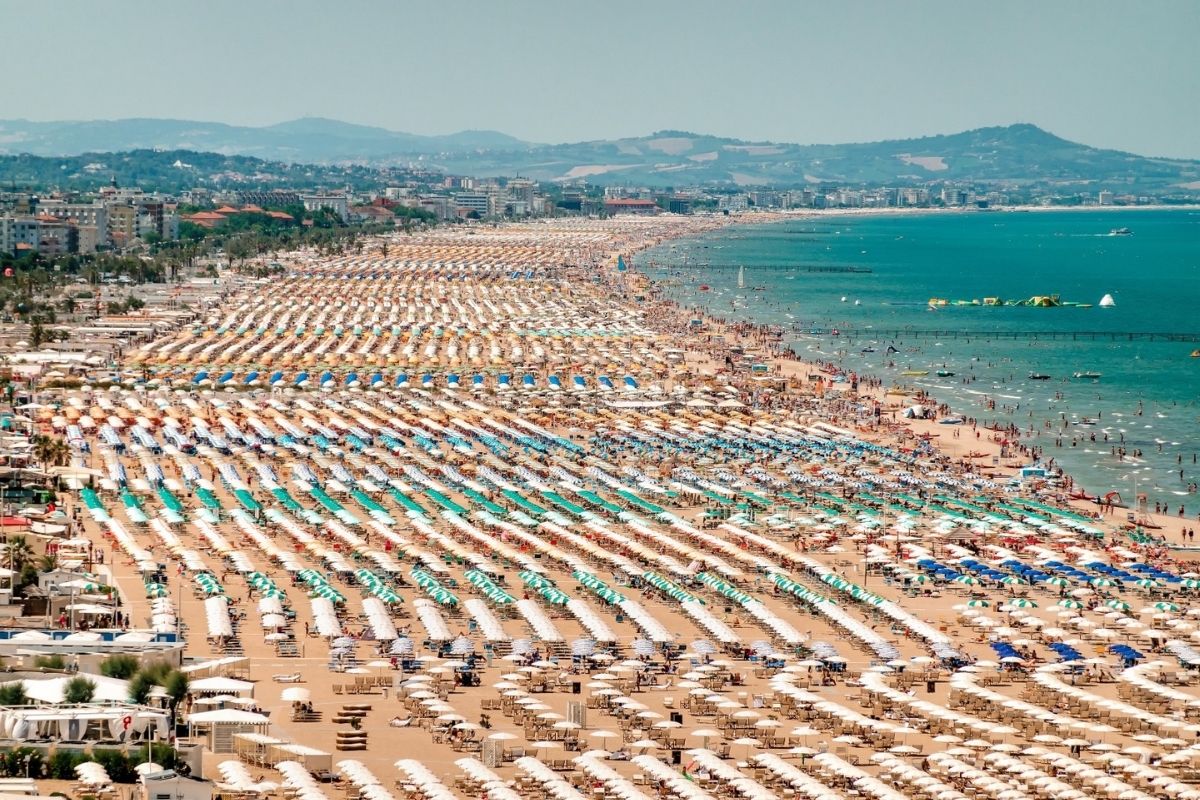 Vista panoramica della spiaggia di Rimini, con il sole al tramonto e i bagnanti.